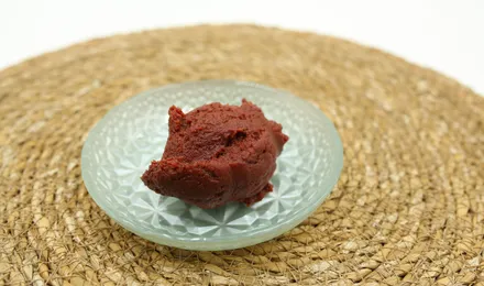 Pâte d'anko brun-rouge lisse et brillante dans un bol en céramique, entourée de haricots azuki secs