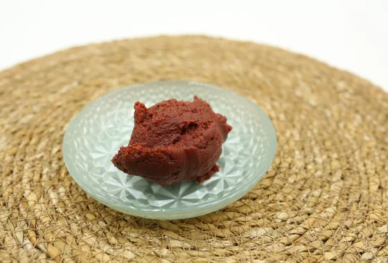 Pâte d'anko brun-rouge lisse et brillante dans un bol en céramique, entourée de haricots azuki secs