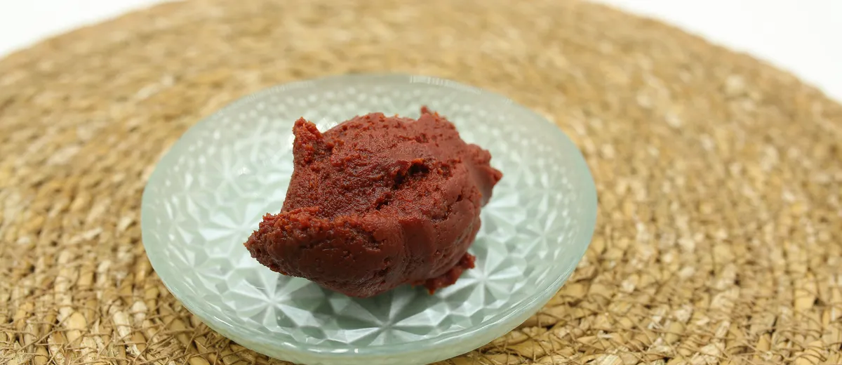 Pâte d'anko brun-rouge lisse et brillante dans un bol en céramique, entourée de haricots azuki secs