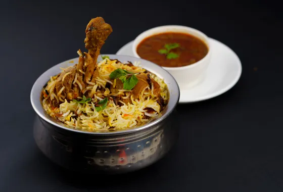 Biryani de poulet hyderabadi, riz basmati safrané et poulet parsemés d'oignons frits, menthe et coriandre dans une marmite