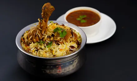 Biryani de poulet hyderabadi, riz basmati safrané et poulet parsemés d'oignons frits, menthe et coriandre dans une marmite