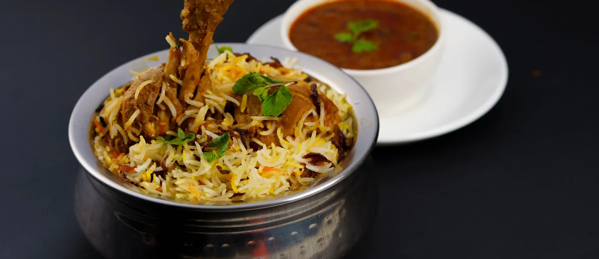 Biryani de poulet hyderabadi, riz basmati safrané et poulet parsemés d'oignons frits, menthe et coriandre dans une marmite