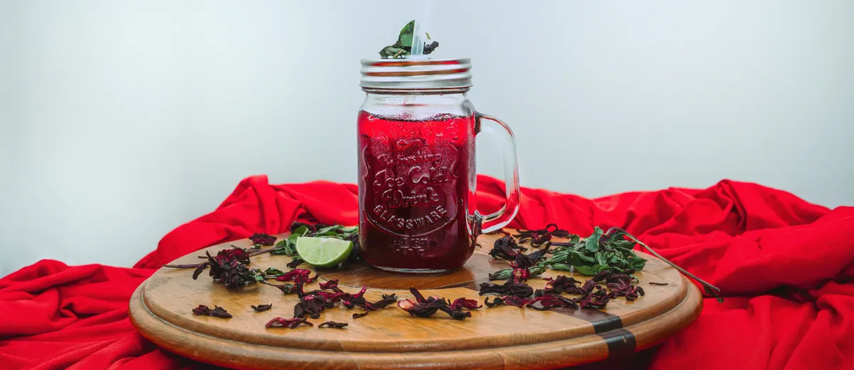 Bissap sénégalais, boisson rouge rubis à l'hibiscus servie dans un verre avec glaçons, feuilles de menthe et tranche de citron.