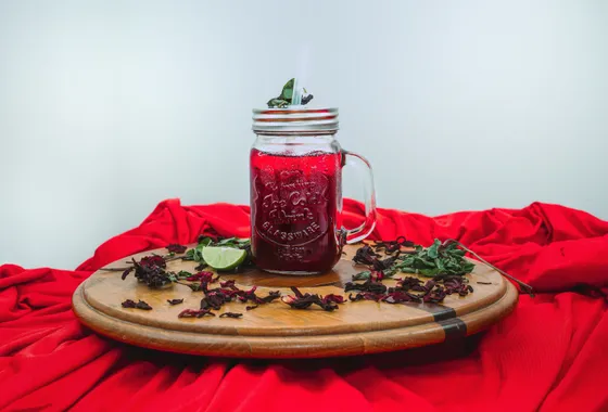 Bissap sénégalais, boisson rouge rubis à l'hibiscus servie dans un verre avec glaçons, feuilles de menthe et tranche de citron.