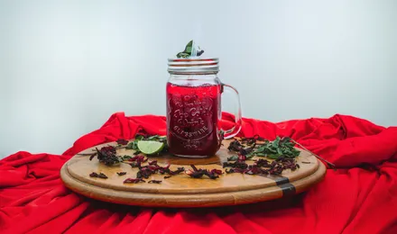 Bissap sénégalais, boisson rouge rubis à l'hibiscus servie dans un verre avec glaçons, feuilles de menthe et tranche de citron.