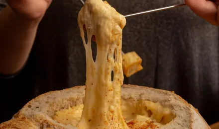 Caquelon de fondue savoyarde filante avec un cube de pain piqué au bout d'une fourchette