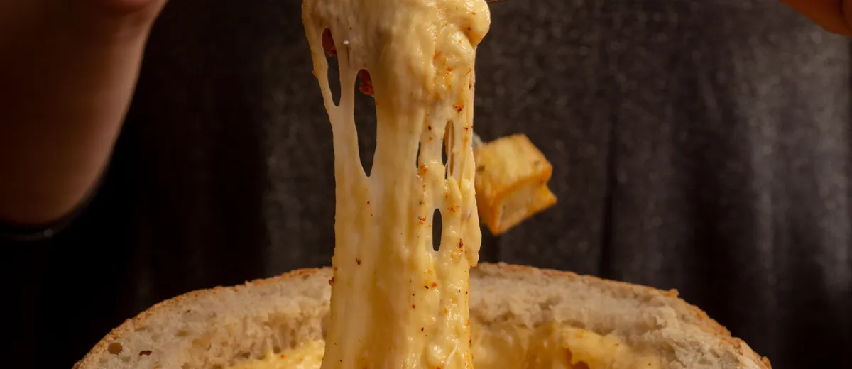 Caquelon de fondue savoyarde filante avec un cube de pain piqué au bout d'une fourchette