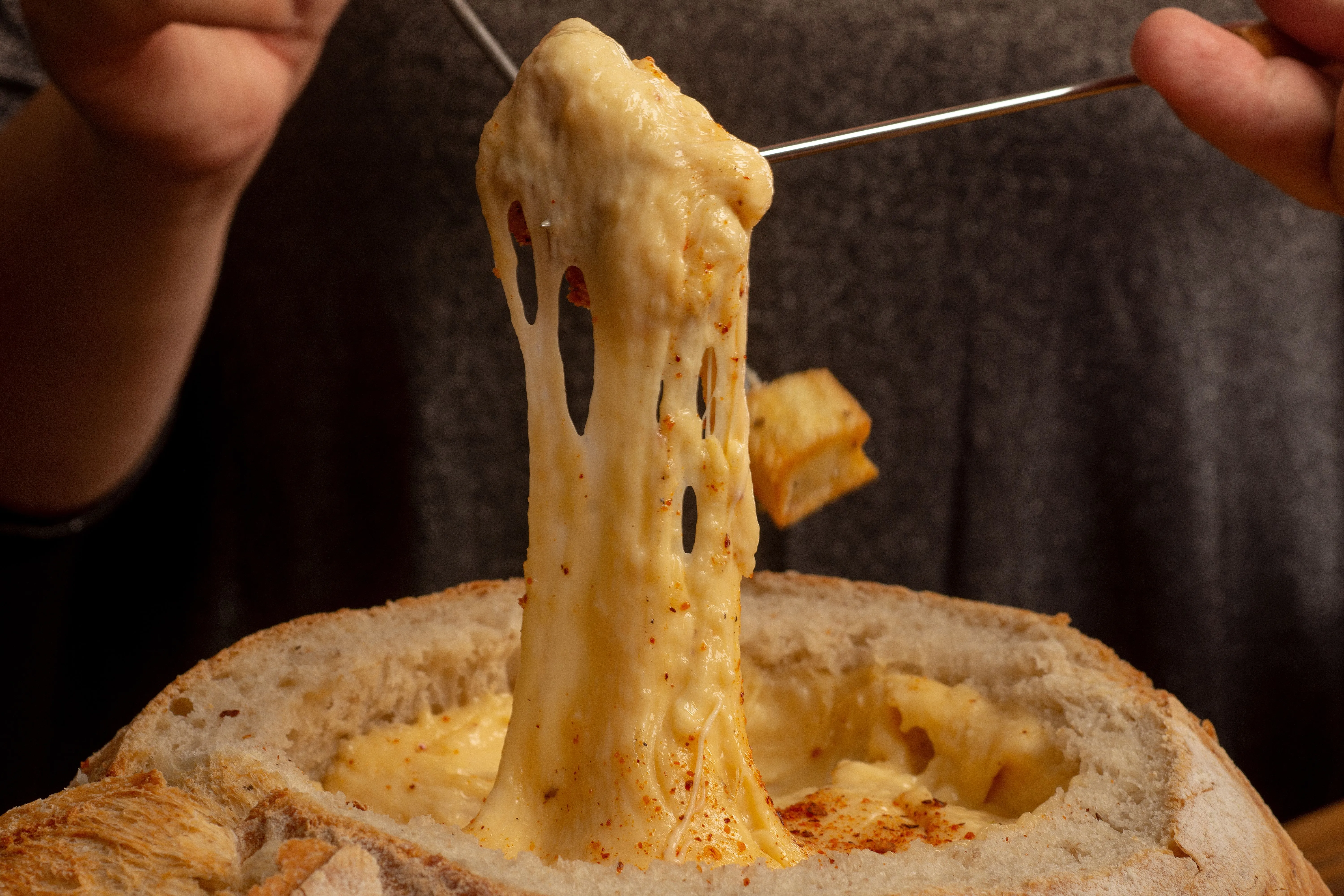 Cube de pain étirant un fil de fromage fondu au-dessus d'un caquelon de fondue savoyarde