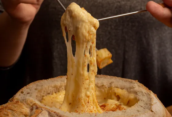 Caquelon de fondue savoyarde filante avec un cube de pain piqué au bout d'une fourchette