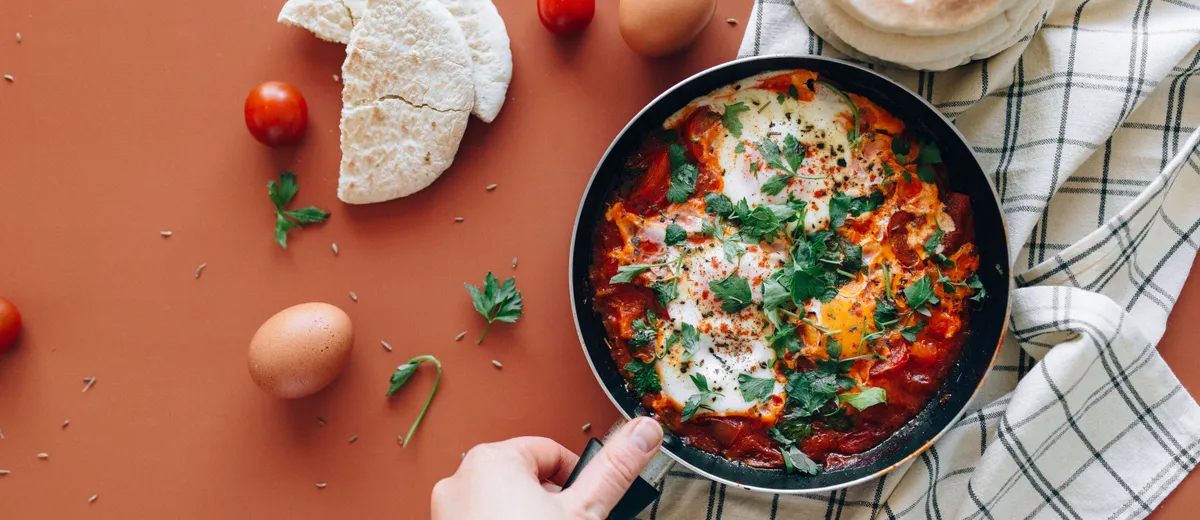 Chakchouka servie dans une poêle en fonte, œufs pochés au jaune coulant sur une sauce de poivrons et tomates parsemée de persil frais