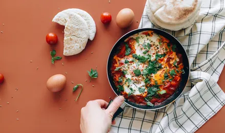 Chakchouka servie dans une poêle en fonte, œufs pochés au jaune coulant sur une sauce de poivrons et tomates parsemée de persil frais