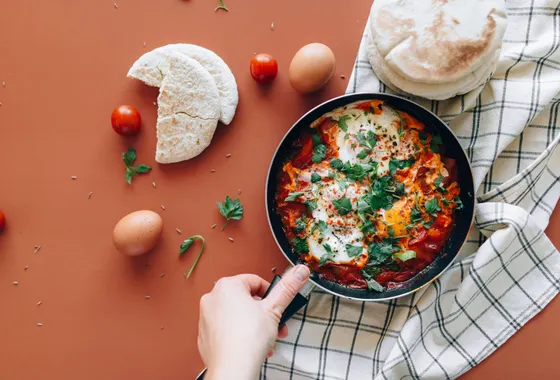 Chakchouka servie dans une poêle en fonte, œufs pochés au jaune coulant sur une sauce de poivrons et tomates parsemée de persil frais