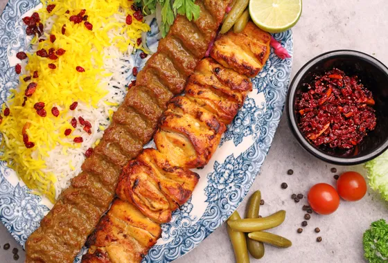 Brochettes de kebab koobideh grillées servies sur un lit de riz basmati safrané avec tomates grillées et sumac.