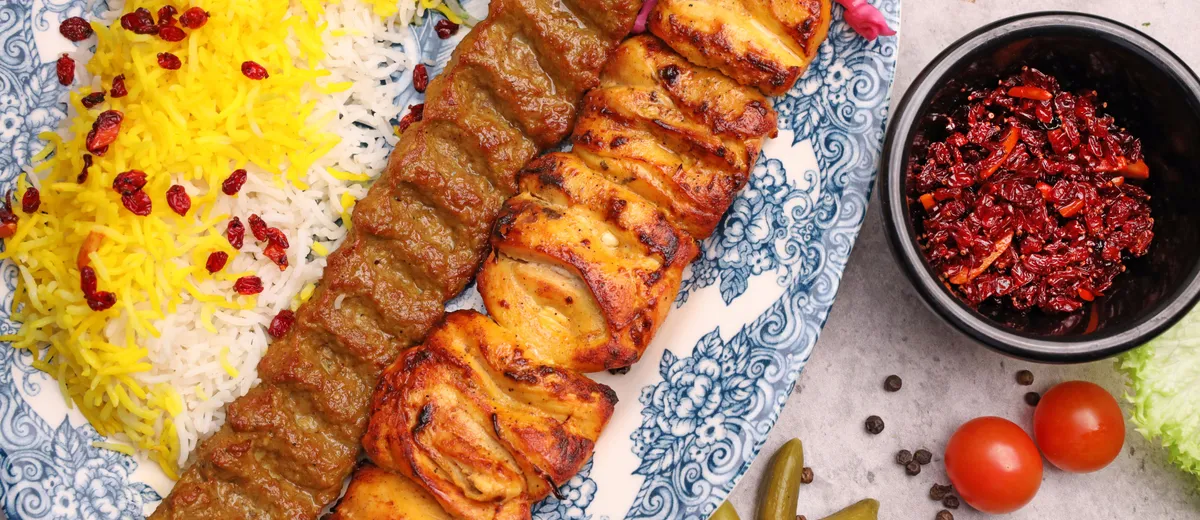 Brochettes de kebab koobideh grillées servies sur un lit de riz basmati safrané avec tomates grillées et sumac.