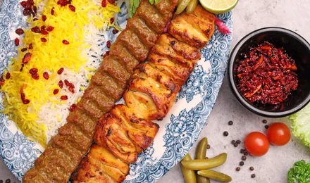Brochettes de kebab koobideh grillées servies sur un lit de riz basmati safrané avec tomates grillées et sumac.