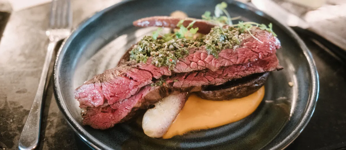 Sauce chimichurri verte dans un bol en verre, persil haché et flocons de piment liés à l'huile d'olive, à côté d'une viande grillée