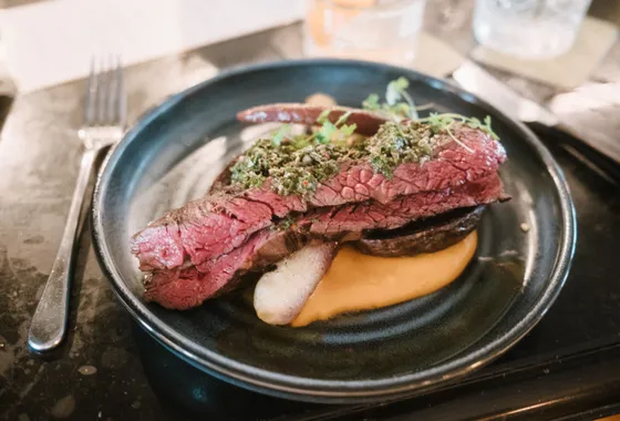 Sauce chimichurri verte dans un bol en verre, persil haché et flocons de piment liés à l'huile d'olive, à côté d'une viande grillée