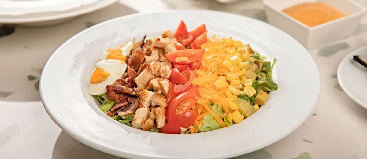 Cobb salad dressée en bandes : poulet, bacon, œuf, avocat, tomates cerises et bleu émietté sur laitue
