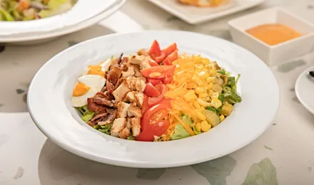 Cobb salad dressée en bandes : poulet, bacon, œuf, avocat, tomates cerises et bleu émietté sur laitue