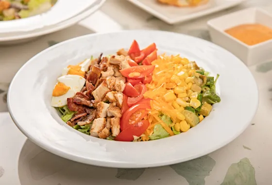 Cobb salad dressée en bandes : poulet, bacon, œuf, avocat, tomates cerises et bleu émietté sur laitue