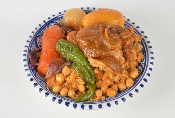 Grand plat de couscous royal, semoule dorée surmontée d'agneau, poulet, merguez et légumes fondants, bouillon parfumé à côté