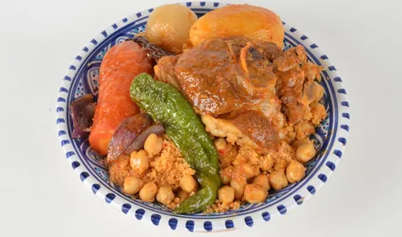 Grand plat de couscous royal, semoule dorée surmontée d'agneau, poulet, merguez et légumes fondants, bouillon parfumé à côté