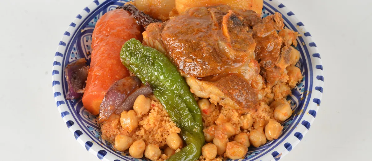 Grand plat de couscous royal, semoule dorée surmontée d'agneau, poulet, merguez et légumes fondants, bouillon parfumé à côté