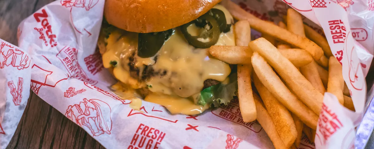 Cheeseburger maison au cheddar fondant et pickles, posé sur du papier kraft à côté d'un panier de frites