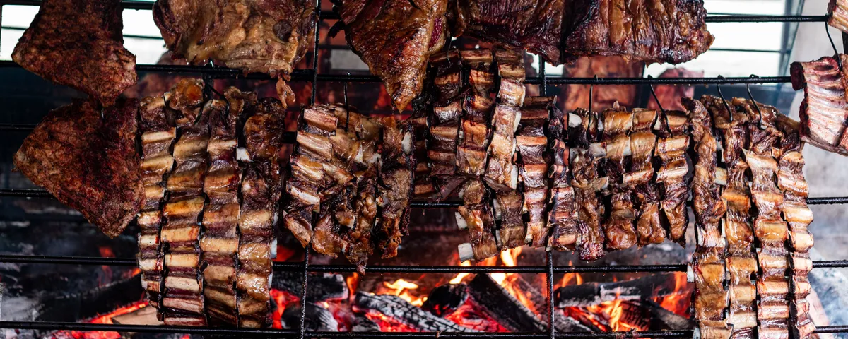 Pièces de bœuf grillant lentement sur une parrilla argentine au-dessus de braises rougeoyantes