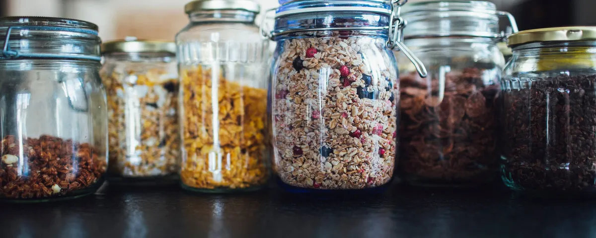 Bocaux de pâte à tartiner, de beurre de cacahuète et de granola maison alignés sur un plan de travail en bois