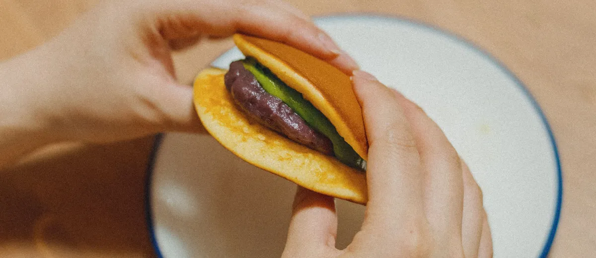 Dorayaki coupé en deux montrant la garniture d'anko brun entre deux pancakes dorés et moelleux, posés sur un plateau en bois.