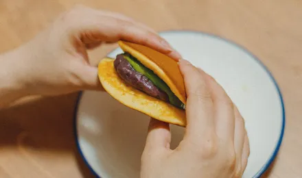 Dorayaki coupé en deux montrant la garniture d'anko brun entre deux pancakes dorés et moelleux, posés sur un plateau en bois.
