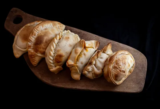 Empanadas argentines dorées au four, chaussons de pâte au bord plissé fourrés de bœuf, posés sur une planche en bois