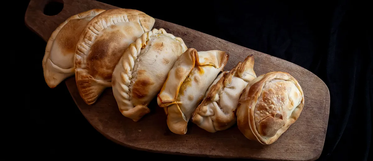 Empanadas argentines dorées au four, chaussons de pâte au bord plissé fourrés de bœuf, posés sur une planche en bois