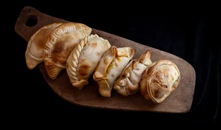 Empanadas argentines dorées au four, chaussons de pâte au bord plissé fourrés de bœuf, posés sur une planche en bois