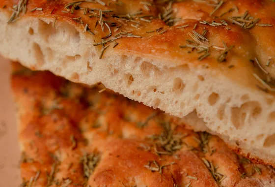 Focaccia italienne dorée parsemée de romarin et de gros sel, marquée de fossettes brillantes d'huile d'olive