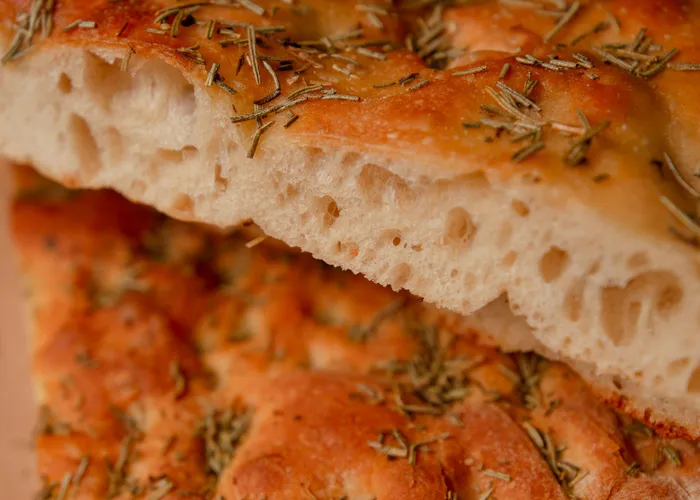 Focaccia italienne dorée parsemée de romarin et de gros sel, marquée de fossettes brillantes d'huile d'olive