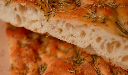 Focaccia italienne dorée parsemée de romarin et de gros sel, marquée de fossettes brillantes d'huile d'olive