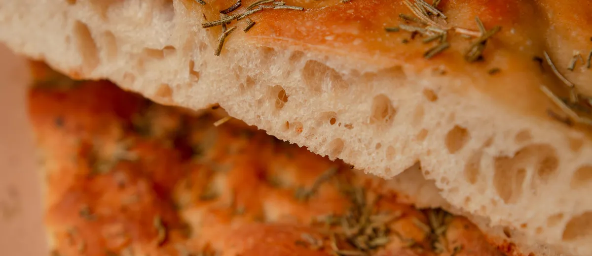 Focaccia italienne dorée parsemée de romarin et de gros sel, marquée de fossettes brillantes d'huile d'olive