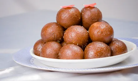 Gulab jamun dorés baignant dans leur sirop ambré parfumé, garnis de pistaches concassées