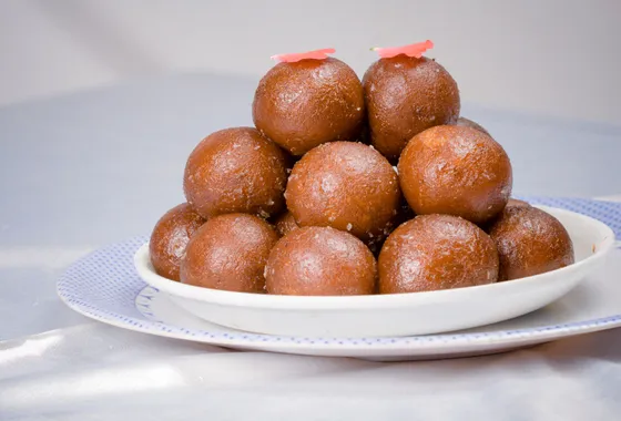 Gulab jamun dorés baignant dans leur sirop ambré parfumé, garnis de pistaches concassées