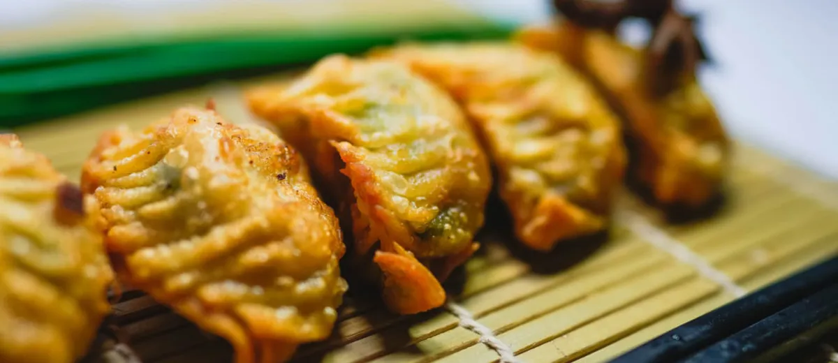 Gyoza japonais dorés à la poêle, alignés en arc de cercle, servis avec un petit bol de sauce soja vinaigrée.