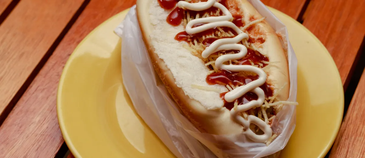 Hot dog garni de saucisse fumée, moutarde, ketchup et oignons dans un pain allongé toasté