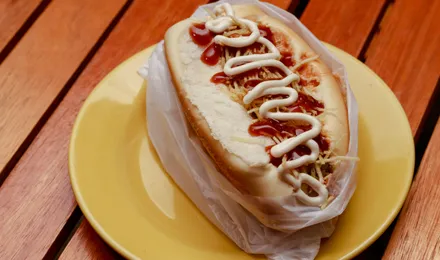 Hot dog garni de saucisse fumée, moutarde, ketchup et oignons dans un pain allongé toasté