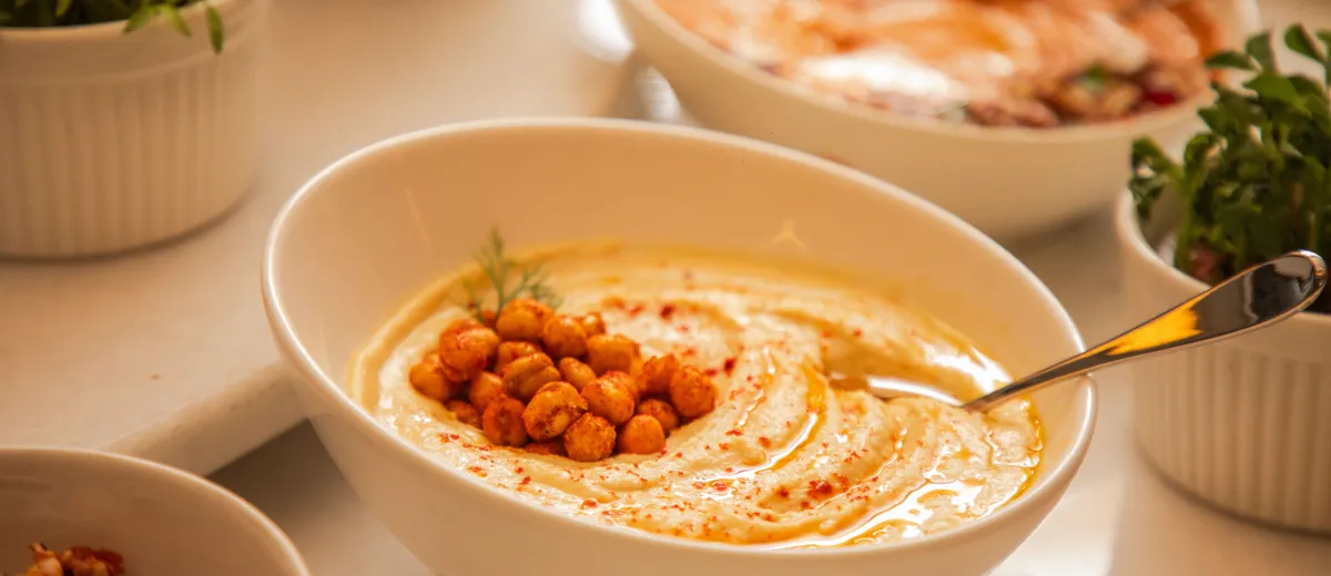 Bol de houmous crémeux nappé d'huile d'olive, saupoudré de paprika et parsemé de pois chiches