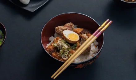 Katsudon dans un grand bol : tranches de porc pané nappées d'œuf coulant sur un lit de riz, parsemées d'oignon vert.