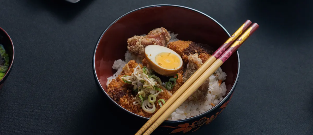 Katsudon dans un grand bol : tranches de porc pané nappées d'œuf coulant sur un lit de riz, parsemées d'oignon vert.