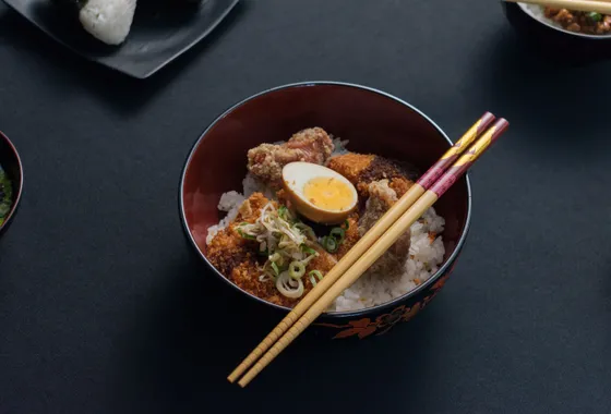Katsudon dans un grand bol : tranches de porc pané nappées d'œuf coulant sur un lit de riz, parsemées d'oignon vert.