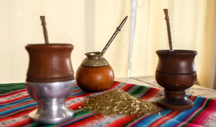 Calebasse de maté remplie de yerba verte avec une bombilla métallique, posée sur une table en bois à côté d'un thermos