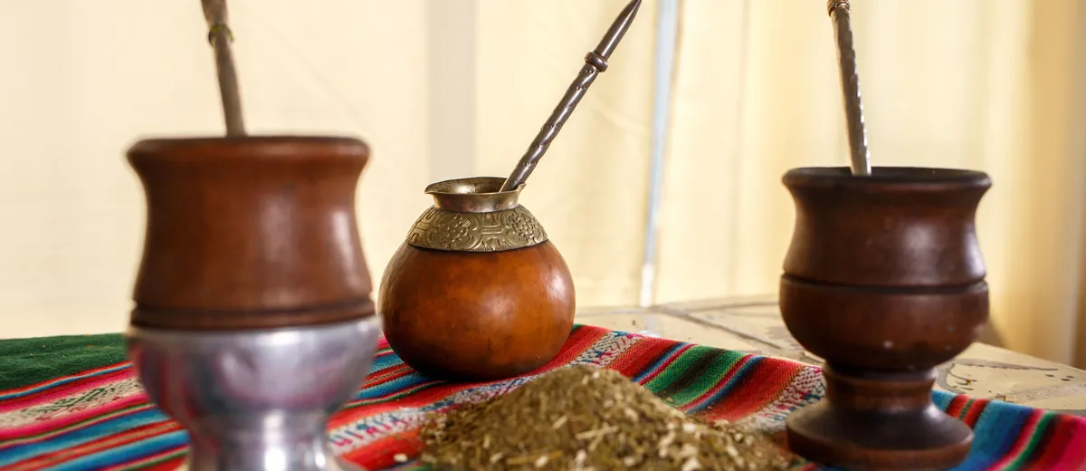 Calebasse de maté remplie de yerba verte avec une bombilla métallique, posée sur une table en bois à côté d'un thermos